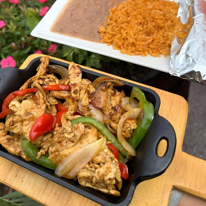 Sizzling chicken fajitas with bell peppers and onions, served with rice and beans at Cafe Bueno.