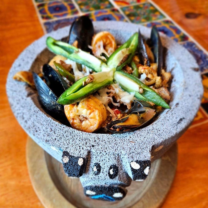 Cafe Bueno's molcajete with mussels, shrimp, cheese, and jalapeños on a colorful tiled table.