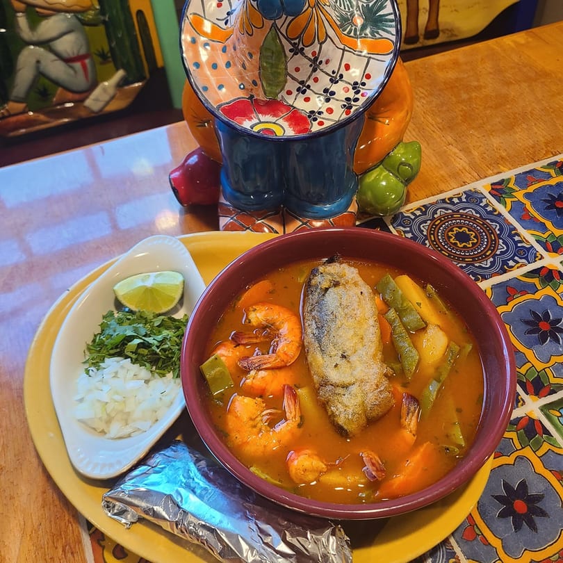 Cafe Bueno's seafood soup with shrimp, fish, and vegetables, served with lime, cilantro, and onions.