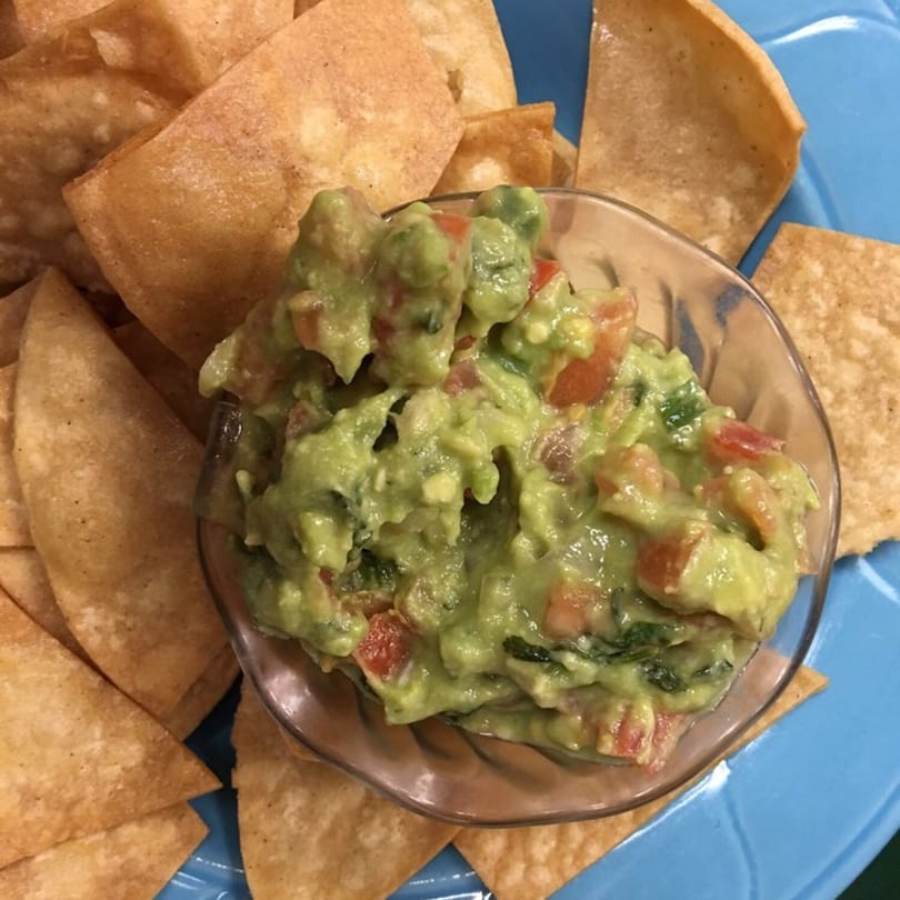 A bowl of chunky guacamole with diced tomatoes and cilantro, surrounded by crispy tortilla chips.